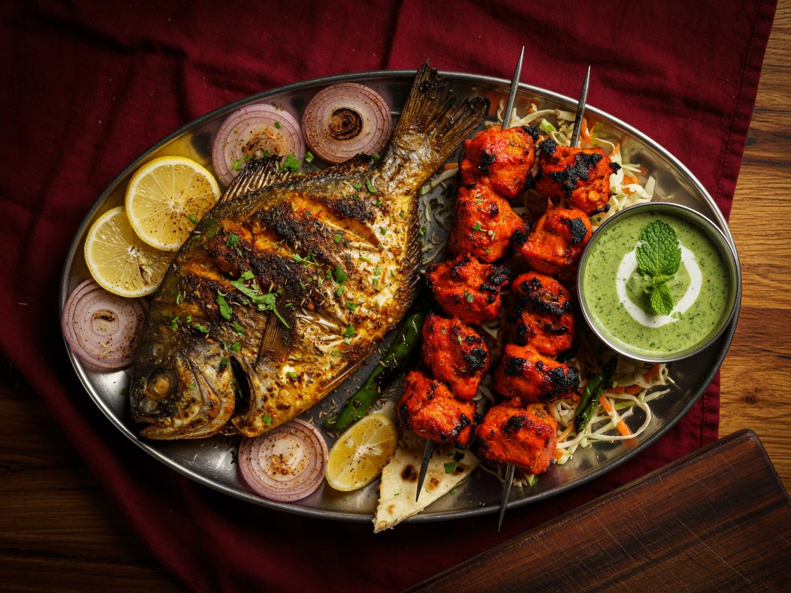 Grilled whole fish and chicken tikka skewers on a steel platter with mint chutney